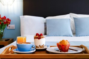 Ein Frühstücksbrett mit einem Glas Orangensaft, einem Joghurt mit Granola und Beeren sowie einem Muffin auf einem Bett mit blauen Kissen.