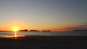 A beach at sunset with silhouettes of people and distant mountains.