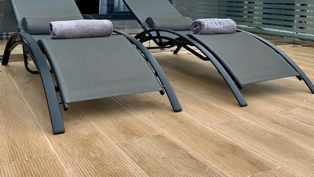 A modern outdoor lounge area with two reclining chairs and a glass balustrade.