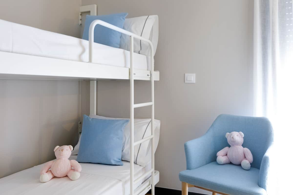 A bunk bed with a ladder, a blue chair, and a pink teddy bear.