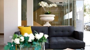 A modern lobby with a dark grey sofa, a yellow pillow, and a vase with white flowers.