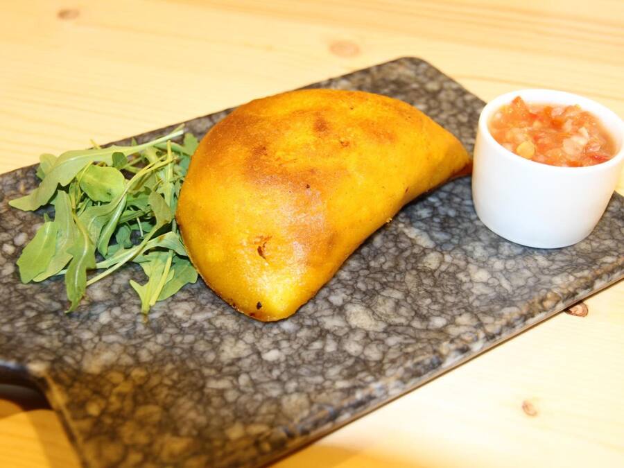A food item on a rectangular plate with a textured surface, accompanied by a small bowl of sauce and some greens.