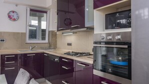 A modern kitchen with dark purple cabinets, stainless steel appliances, and a built-in oven. - Apartment in Arbanija with bubble bath (Trogir - Arbanija)