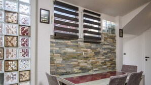 A dining area with a glass table and chairs, a stone wall, and a window with patterned glass. - Apartment in Arbanija with bubble bath (Trogir - Arbanija)