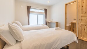 A hotel room with two beds, a wooden wardrobe, a small desk, and a window with curtains. - Lodge Mori Apartments (Kutchan)