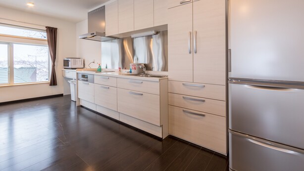 A modern kitchen with light-colored cabinets, stainless steel appliances, and a large window with curtains. - Lodge Mori Apartments (Kutchan)