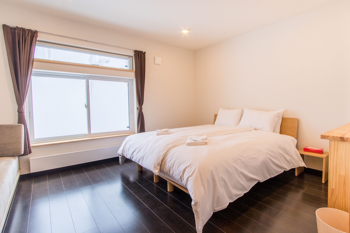 A bedroom with a large bed, a wooden nightstand, a radiator, and a window with curtains.