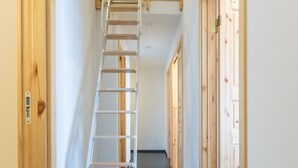 A hallway with a wooden door on the left, a white ladder leading to a loft, and a wooden door on the right. - Lodge Mori Apartments (Kutchan)