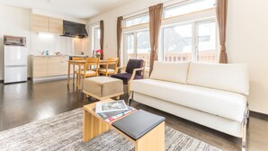 A modern living room with a white sofa, a coffee table, and a dining area with wooden furniture. - Lodge Mori Apartments (Kutchan)