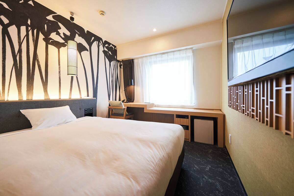 A hotel room with a large bed, a desk, and a window with curtains.