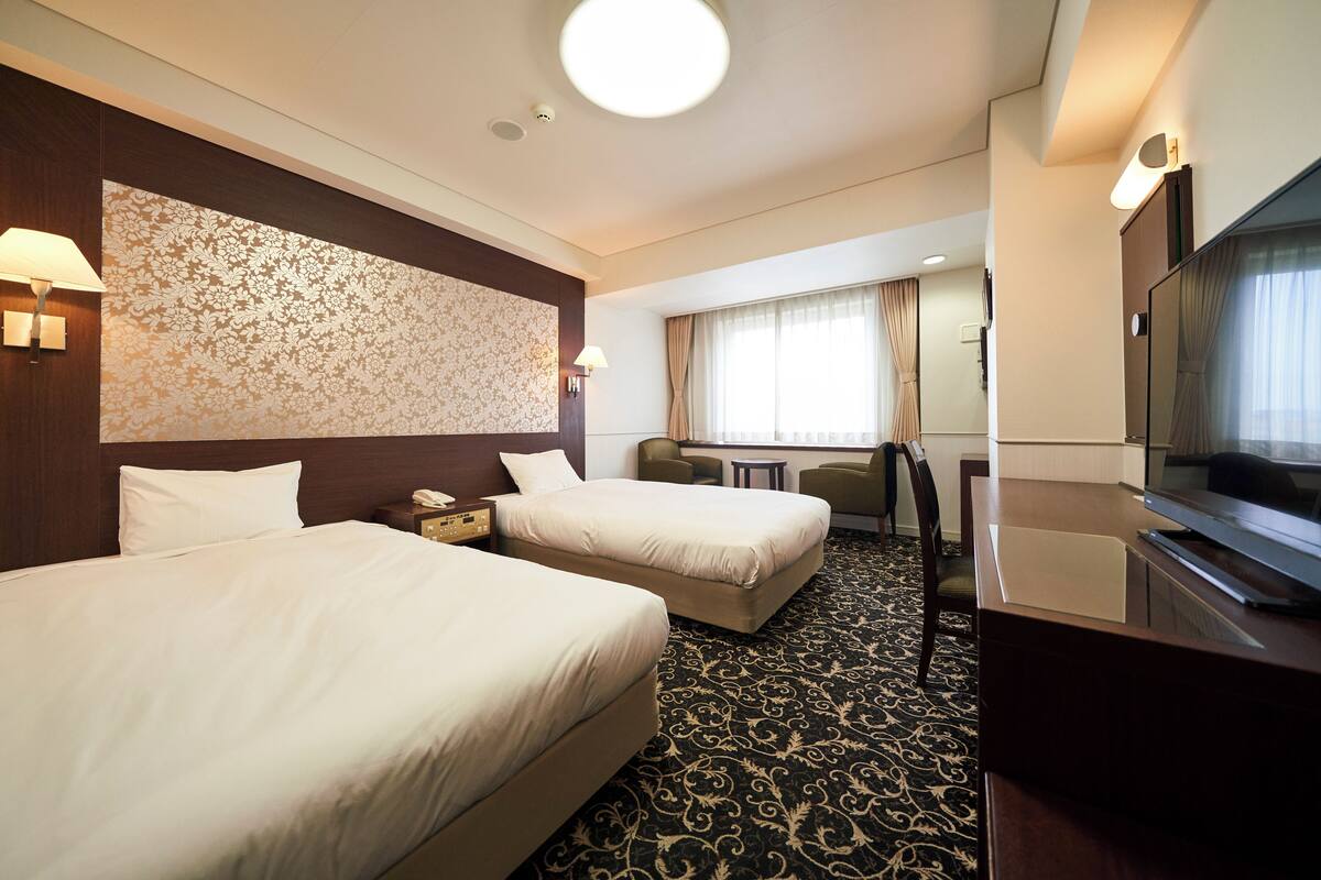A hotel room with two beds, a desk, a television, and a patterned carpet.