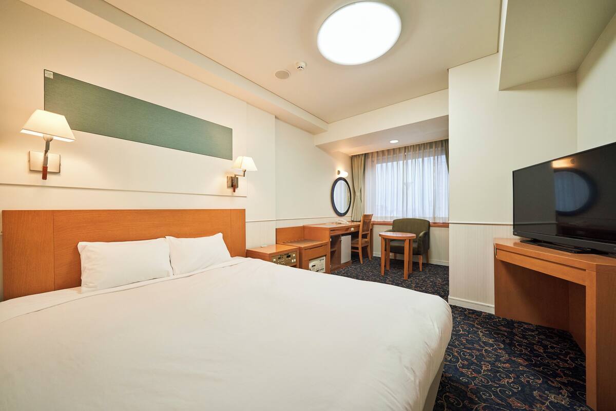 A hotel room with a large bed, a desk, a chair, a television, and a mirror.