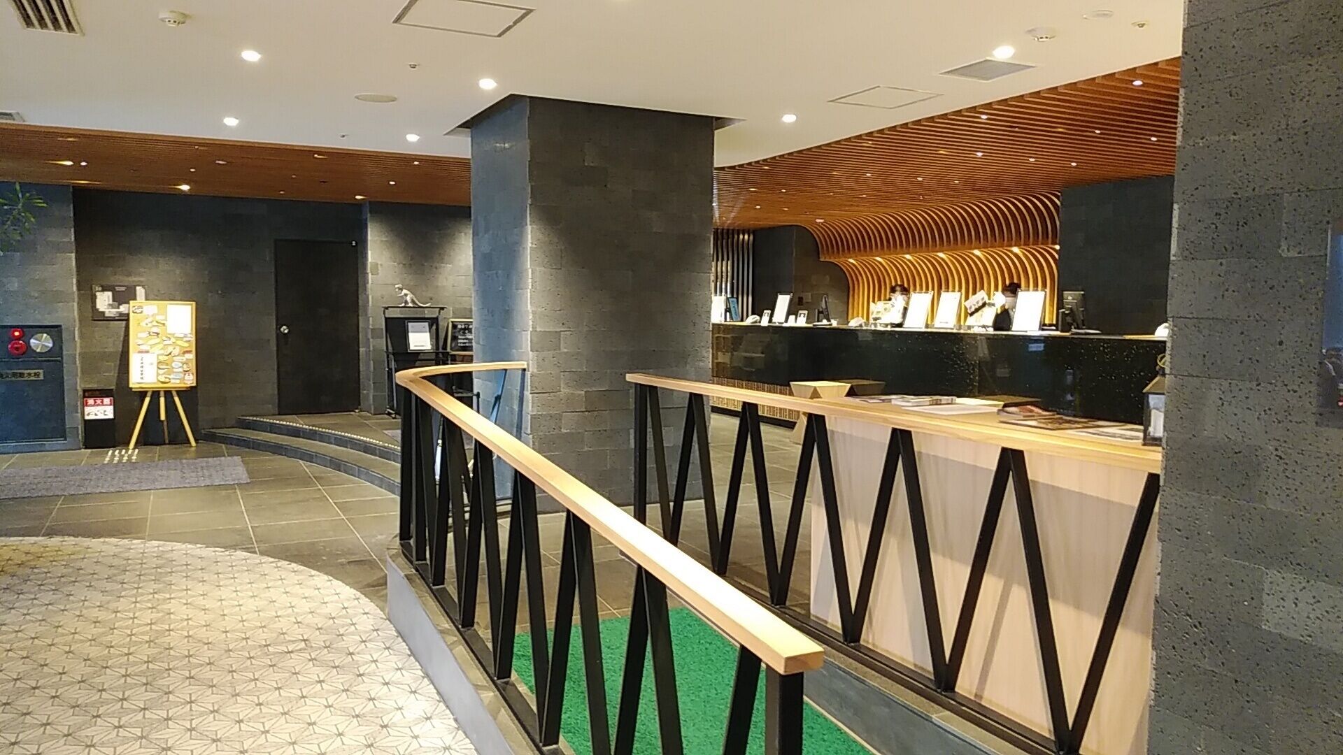 Zona de recepción con mostrador, panel informativo y una escalera que conduce a otro piso.