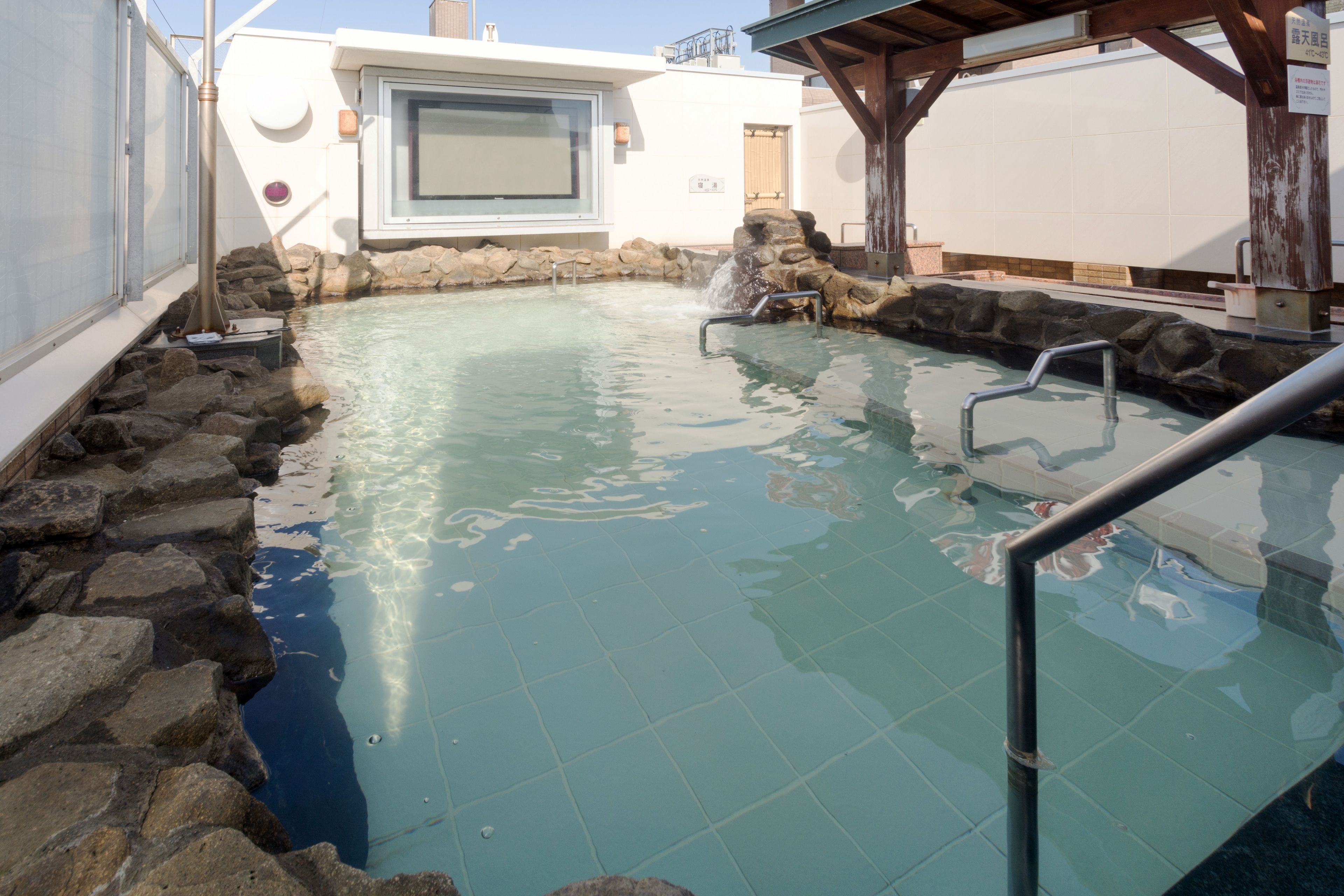 Una piscina cristalina con borde de piedra, cubierta de madera y escalera de metal.