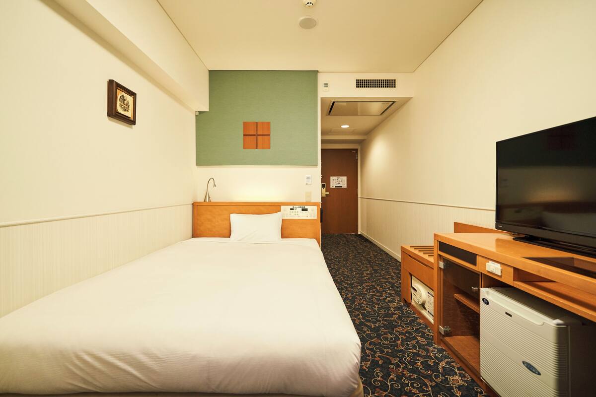 A hotel room with a bed, a television, a desk, and a small refrigerator.