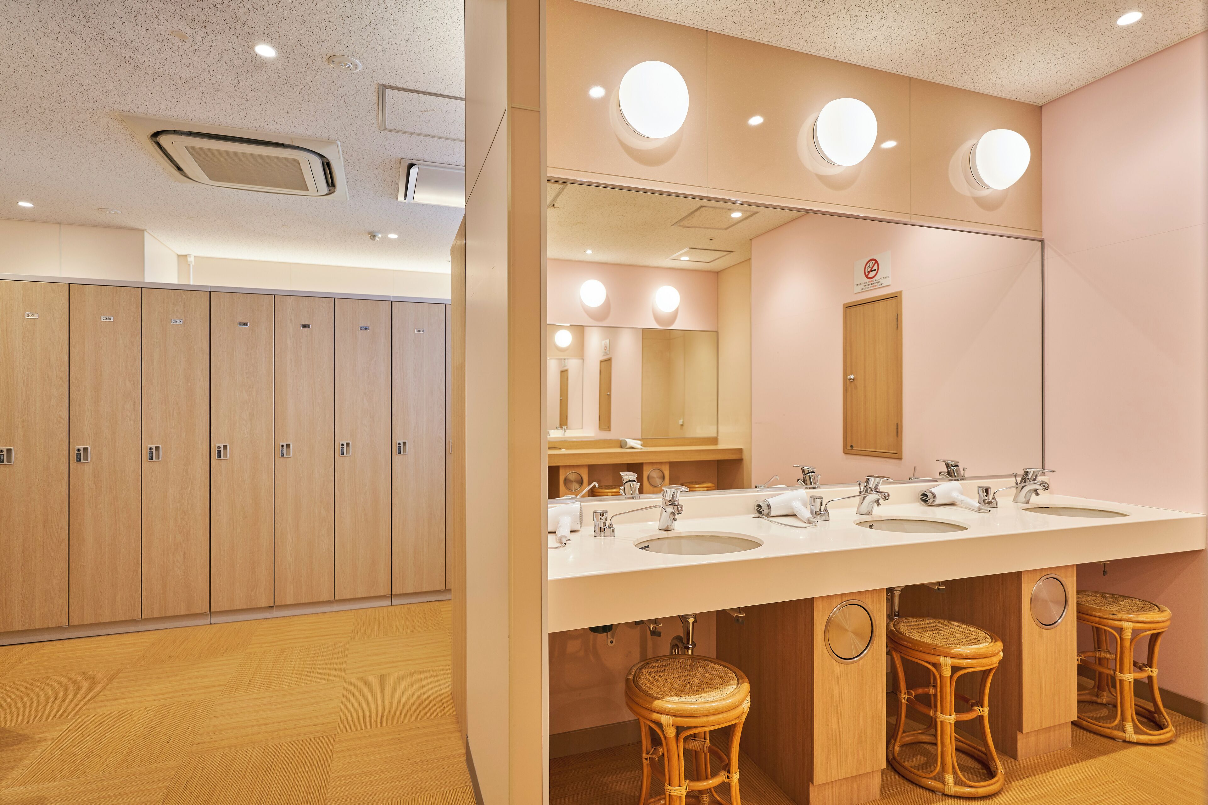 A modern bathroom with wooden lockers, a large vanity with three sinks, and a mirror above the sinks.