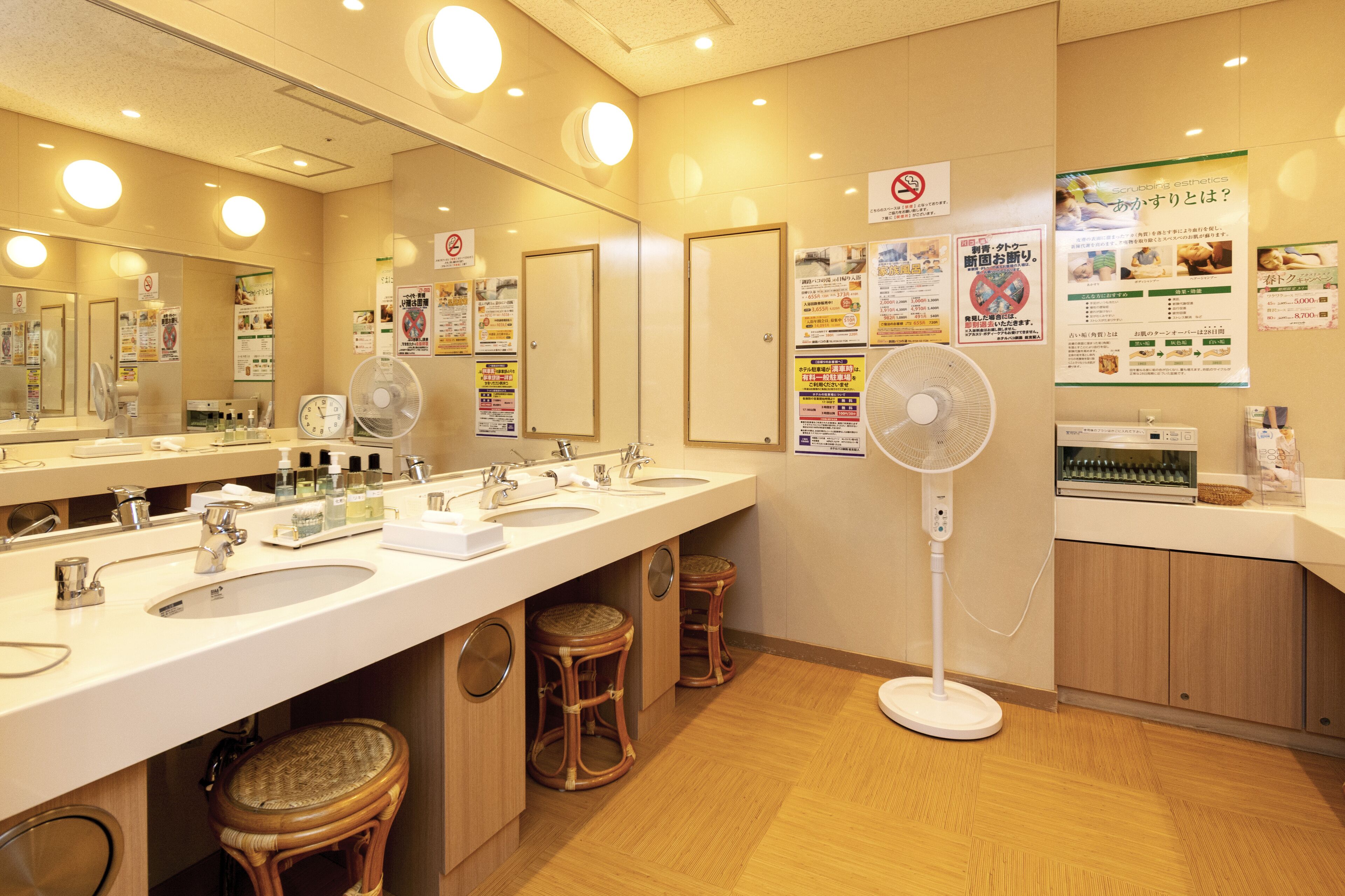 A hotel bathroom with two sinks, a large mirror, and a fan.