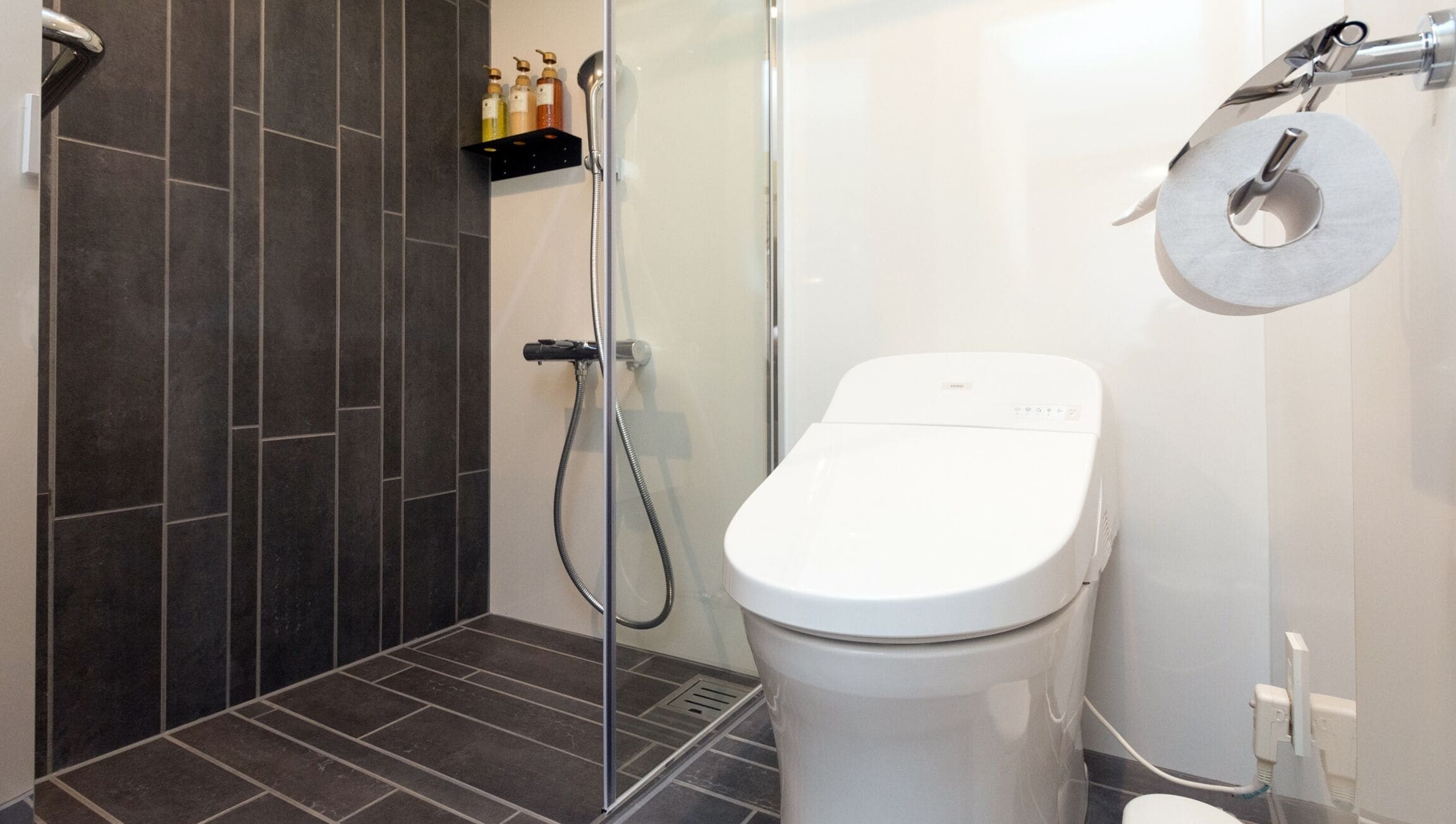 A modern bathroom with a glass shower enclosure, a white toilet, and a shelf with toiletries.