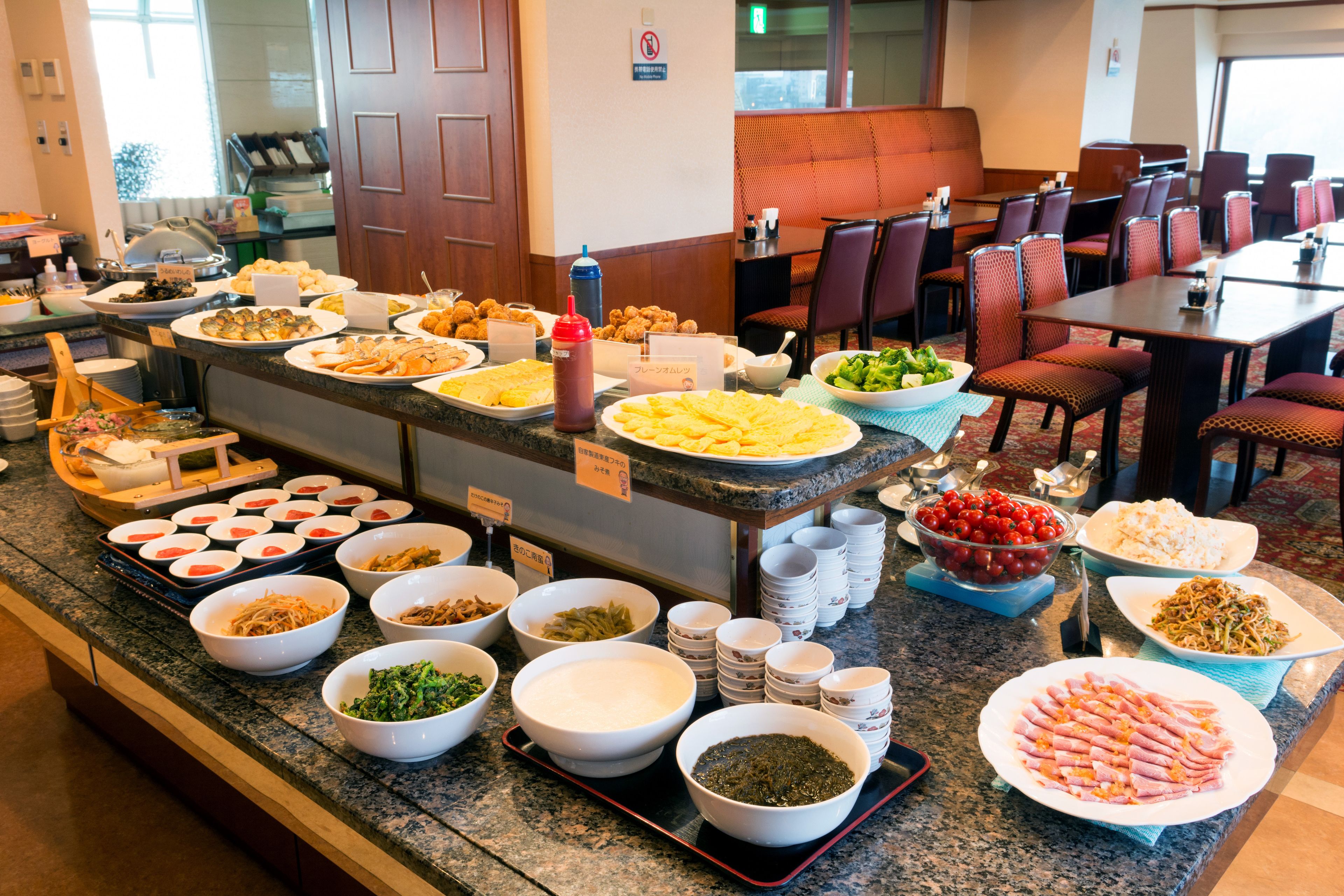A buffet with various dishes and a seating area with tables and chairs.