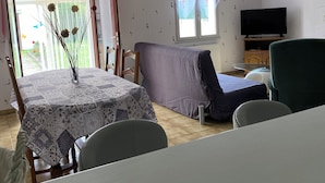 Una habitación con una mesa de comedor, un sofá, un televisor y una ventana con cortinas.