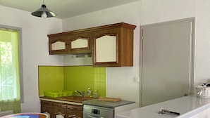 Cocina compacta con armarios de madera, lavavajillas, salpicadero verde y una pequeña mesa de comedor.