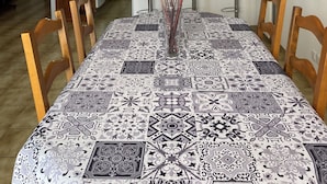Un comedor con mantel estampado, sillas de madera y un florero con flores.