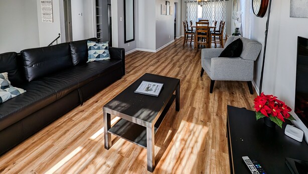 A living room with a black leather sofa, a grey armchair, a wooden coffee table, and a dining area with a wooden table and chairs.