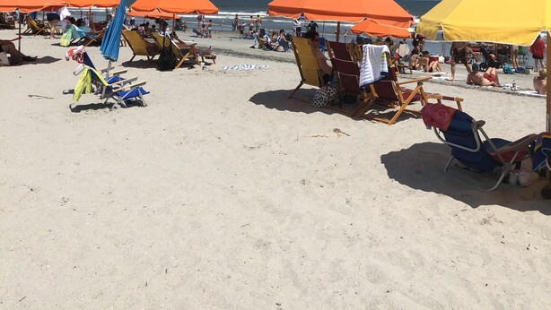 En strand med flera orangefärgade parasoller som ger skugga, och ett antal strandstolar och handdukar utlagda för besökarna.