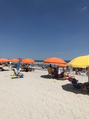 A beach with multiple orange umbrellas providing shade, and several beach chairs and towels laid out for visitors.