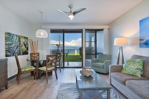 Ein modernes Wohnzimmer mit Glastisch, Holzstühlen, einer Couch und einem Deckenventilator.