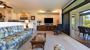 A spacious living room with a sofa, coffee table, and a flat-screen TV. There is a dining area with chairs and a table, and a balcony with outdoor seating. - Amazing Views; Walk to Kaanapali Beach and Whaler Village - Kaanapali Royal N102 (Lahaina)