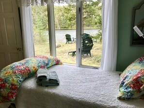 A bedroom with a bed, floral pillows, and a view of an outdoor area with chairs and a table.