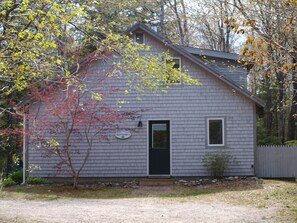 A small, single-story building with a gray exterior, a black door, and a small window.