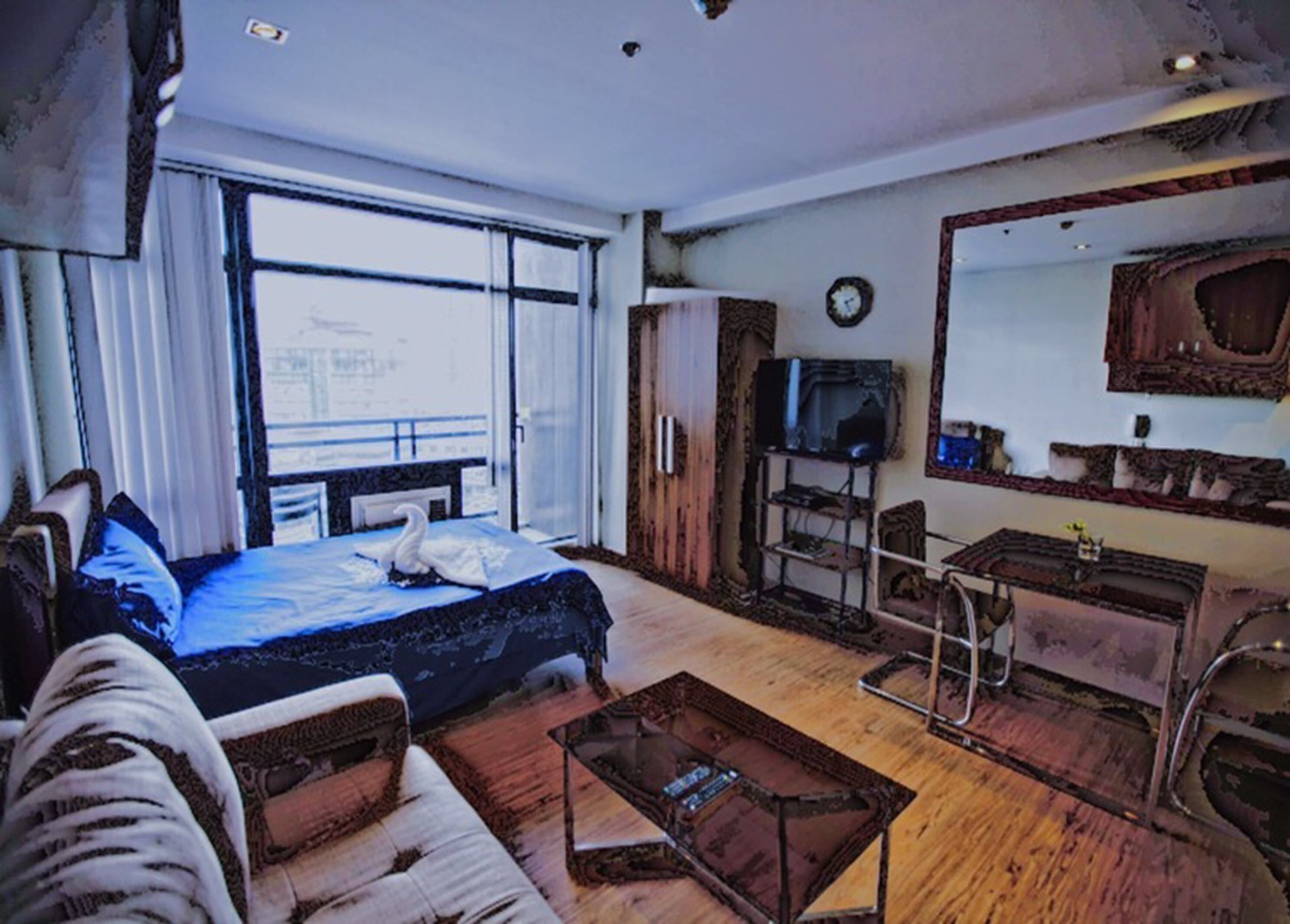 A hotel room with a large bed, a sofa, a coffee table, a TV, and a wardrobe.