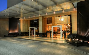 En modern hotellentrén med en glasfasad, en receptionsdisk och en sittgrupp utomhus.