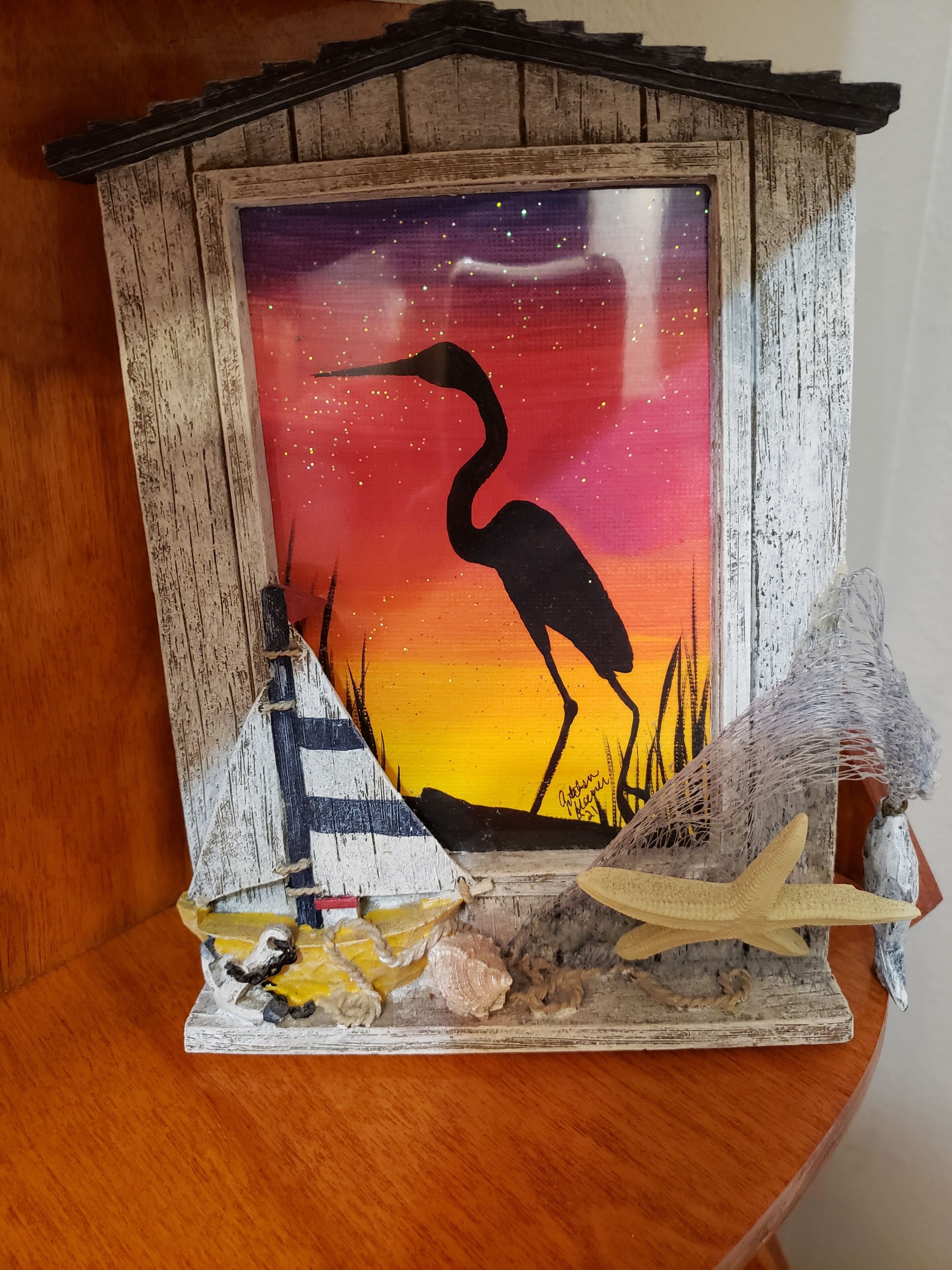 A rustic wooden cabinet with a framed painting of a bird silhouette against a sunset.