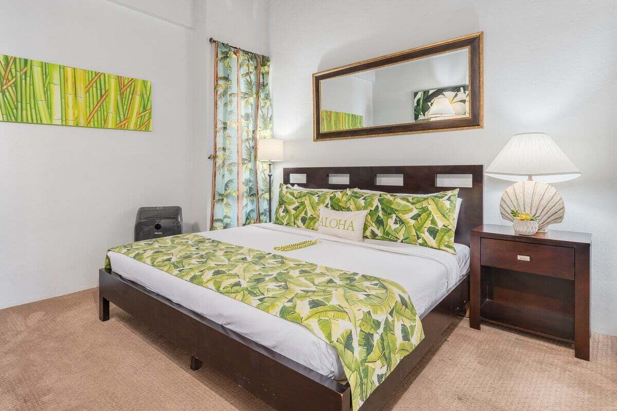 Une chambre d’hôtel avec un lit, une table de chevet, une lampe, un miroir et un mur orné d’un tableau encadré.