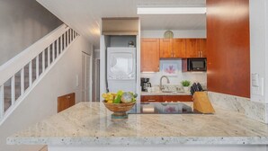 Una cocina moderna con encimera de mármol, electrodomésticos de acero inoxidable, armarios de madera y horno empotrado.