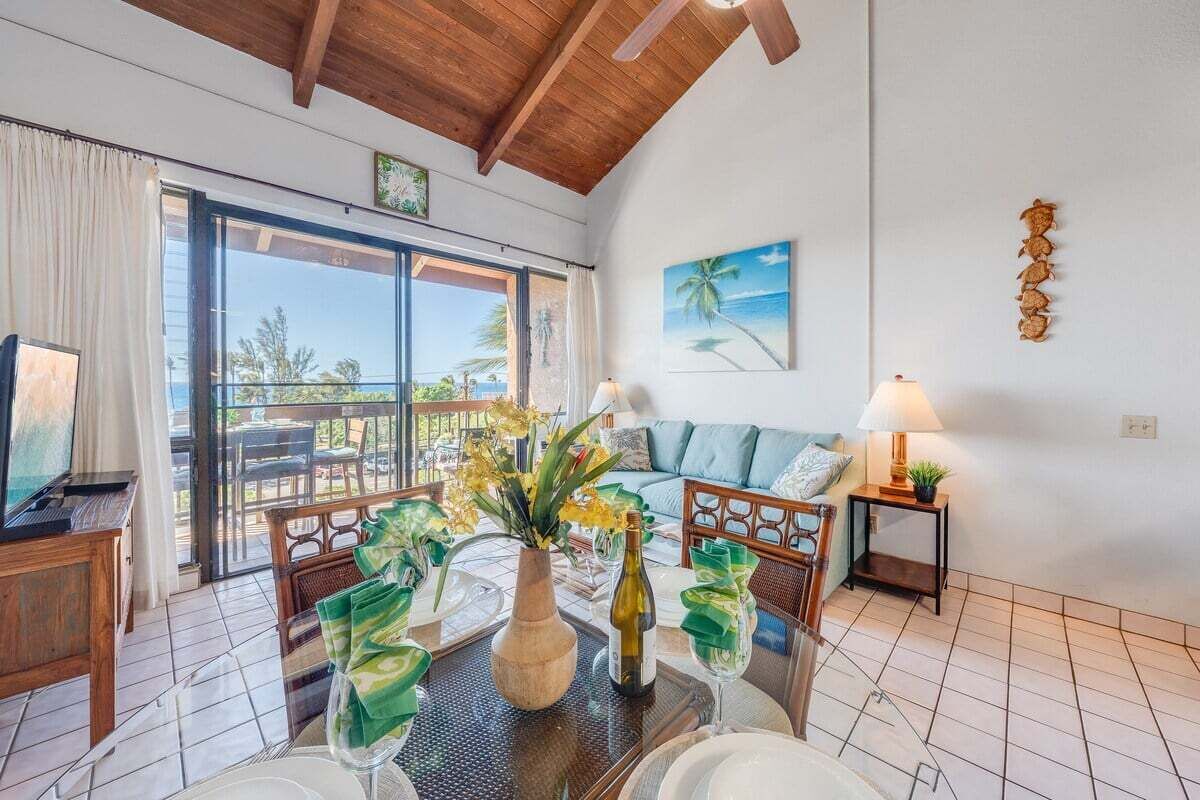 Een ruime woonkamer met een grote schuifpui naar een balkon, een houten plafond, een bank, een salontafel met decoratieve objecten, en een tv op een houten dressoir.
