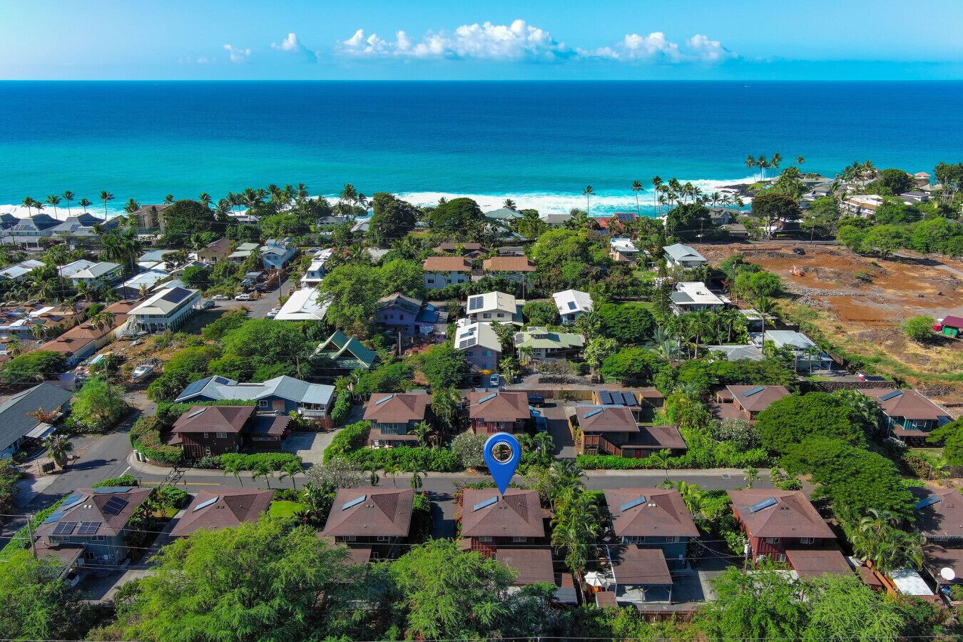 Vista aérea de una zona residencial con casas, algunas con paneles solares, y vista al océano.