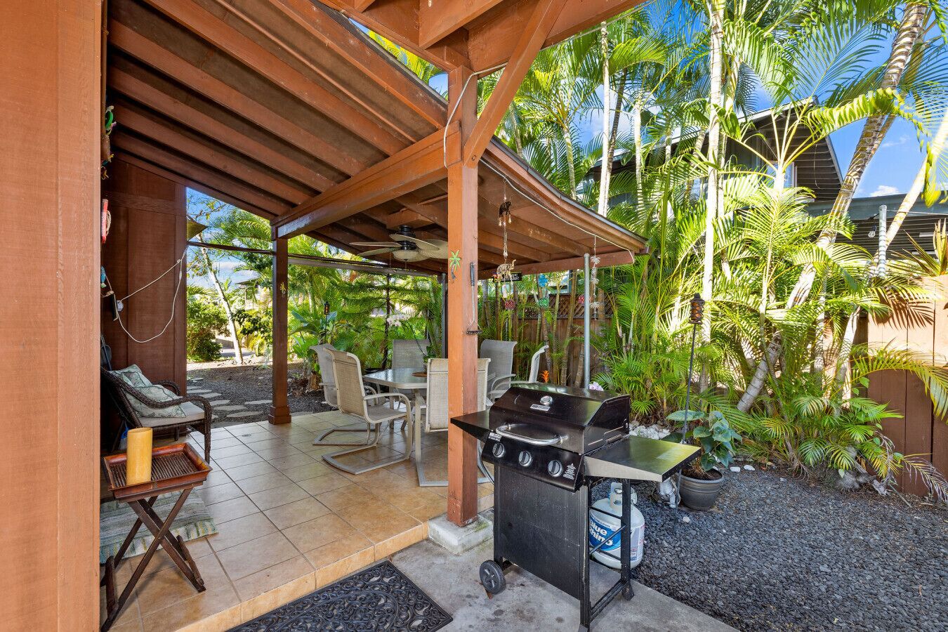 An outdoor patio with a grill, seating, and tropical plants.
