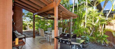 An outdoor patio with a grill, seating, and tropical plants.