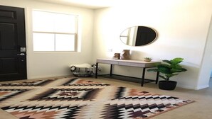 A clean, modern entryway with a dark door, a large window, a console table with a mirror, a potted plant, and a patterned rug. - RELAXING INDIAN PALMS HOME WALK TO POLO FIELDS, PRIVATE POOL! ON GOLF COURSE (Indio)