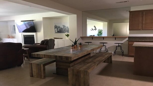 A modern living room with a wooden dining table, a sofa, and a TV. There is a kitchen area with a countertop and stools. - RELAXING INDIAN PALMS HOME WALK TO POLO FIELDS, PRIVATE POOL! ON GOLF COURSE (Indio)