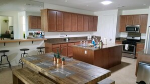 A modern kitchen with wooden cabinets, a central island, and a dining area with a bench. - RELAXING INDIAN PALMS HOME WALK TO POLO FIELDS, PRIVATE POOL! ON GOLF COURSE (Indio)