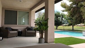A covered patio area with two wicker sofas, a potted plant, and a view of a swimming pool. - RELAXING INDIAN PALMS HOME WALK TO POLO FIELDS, PRIVATE POOL! ON GOLF COURSE (Indio)
