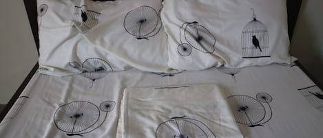 A bed with a white sheet featuring black bicycle and bird designs, a matching pillow, and a neatly folded blanket.