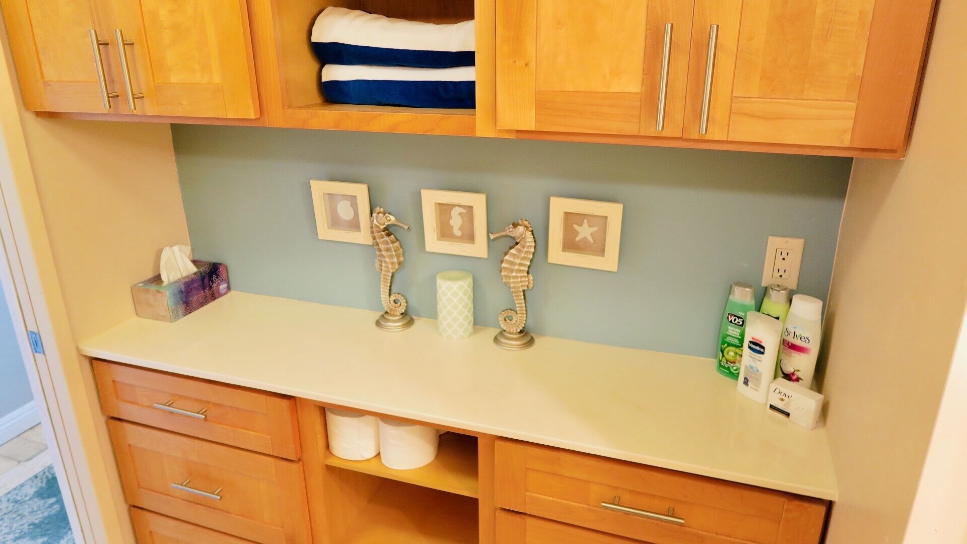 A bathroom with wooden cabinets, a white countertop, and a shelf with toiletries.