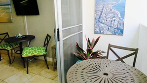 Zona de menjador amb taula rodona i cadires, televisió penjada a la paret i un quadre amb una vista urbana.