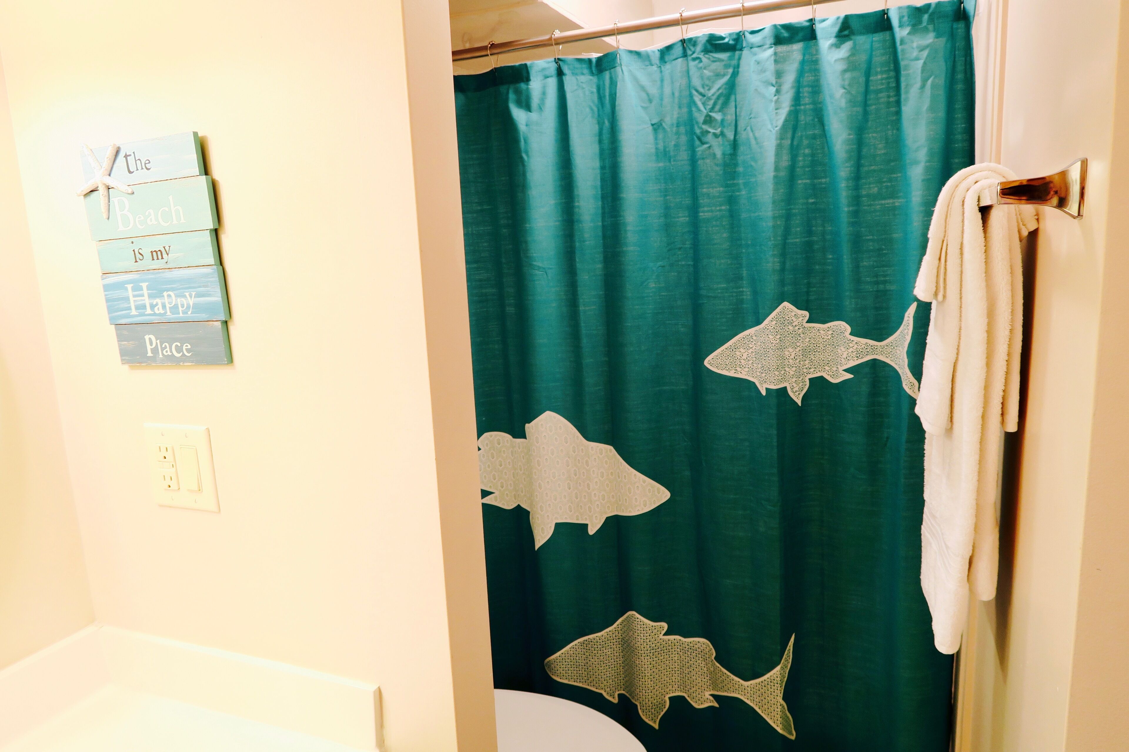 A bathroom with a teal shower curtain featuring shark designs, a towel rack, and a sign on the wall.